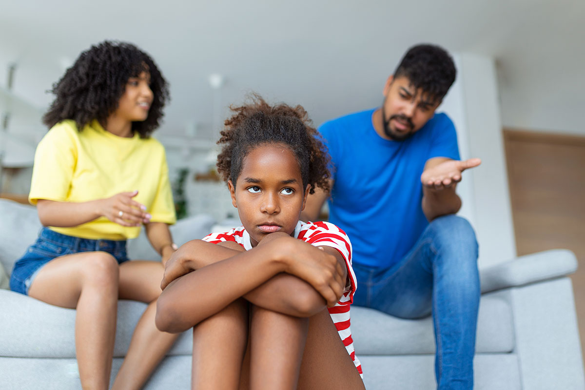 Two parents arguing with an annoyed-looking girl.