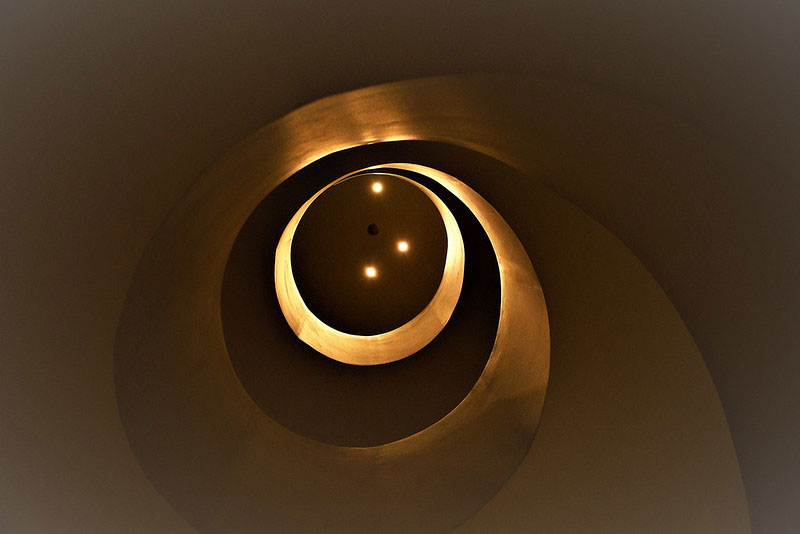 An ever-decreasing spiral of gold against black, like a snails shell - but it is a modern-style spiral staircase looking up